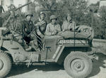 Servicemen and women standing behind a jeep by Unknown